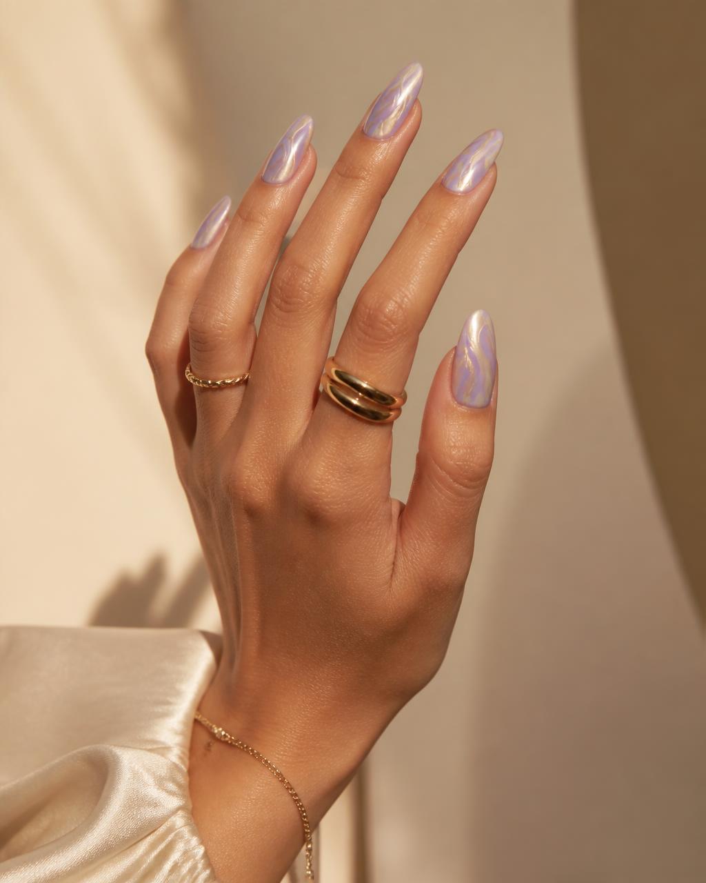 Hand with sculpted lavender chrome nail art against a warm cream backdrop
